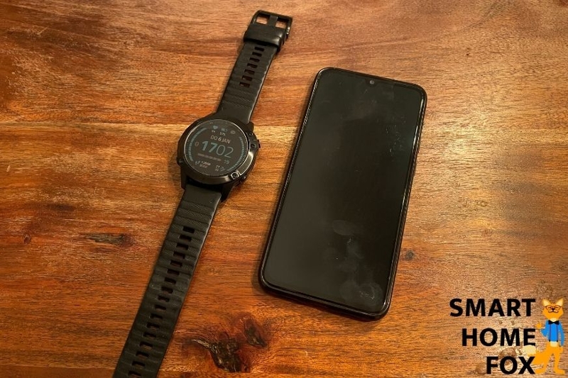 A smartphone and fitness watch placed beside each other.